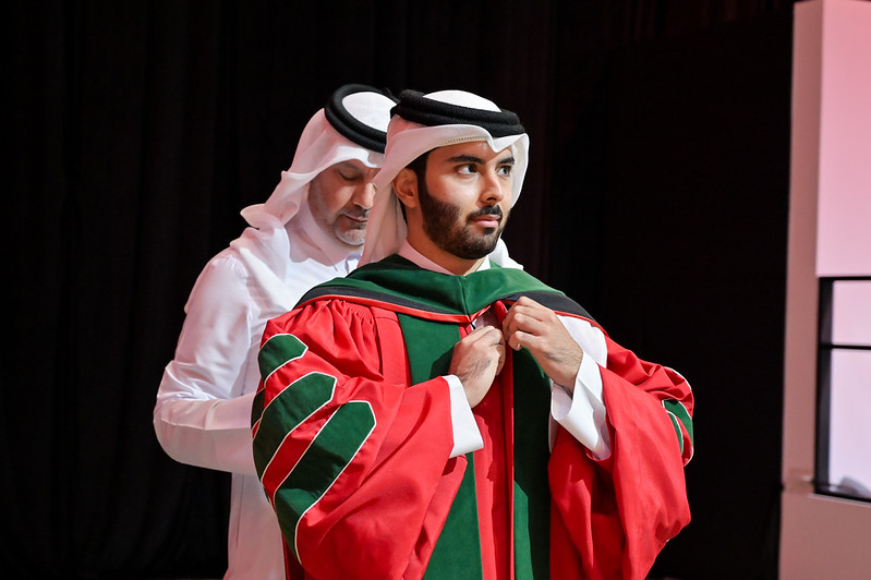 A male student has the hood of his regalia attached by his father