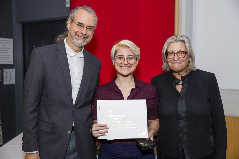A student receives an award surrounded by two associate deans