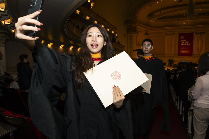 A grad student in regalia takes a photo with her diploma envelope