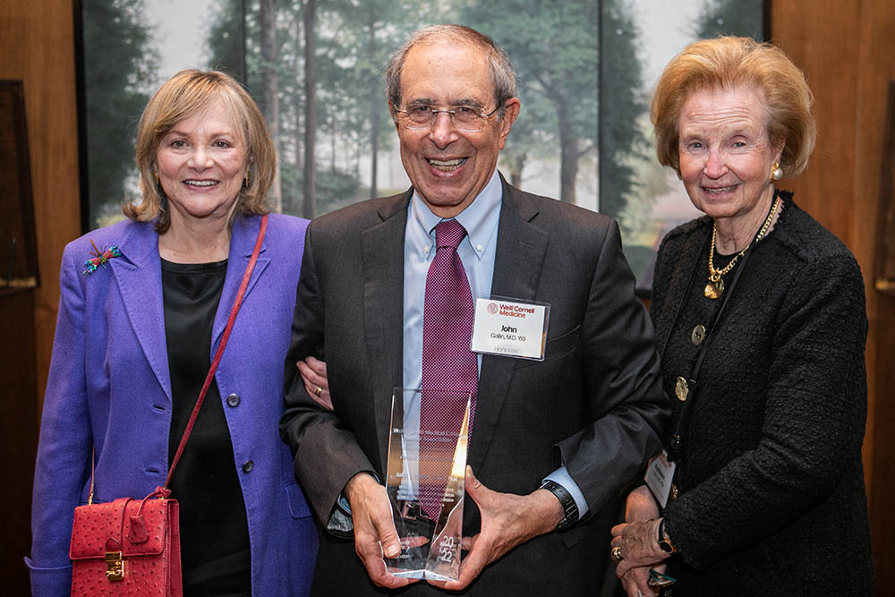 Dr. John Gallin, alongside his wife Dr. Elaine Gallin (left) accepts his award from Dr. Kathleen M. Foley (right)