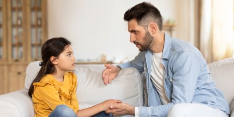 A father speaks with his daughter on a couch
