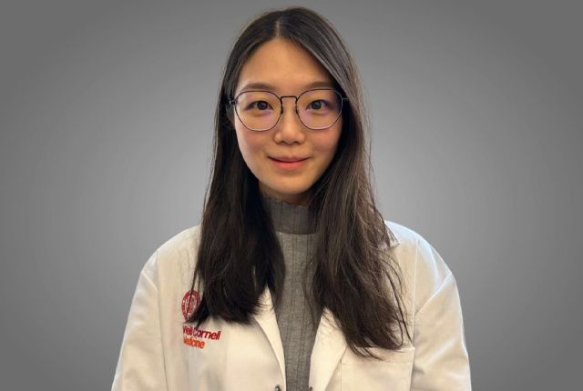 An East Asian woman with long black hair and glasses wearing a white coat