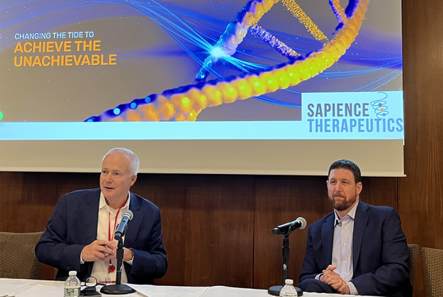Two Caucasian men in suits sitting at a table and looking at the audience